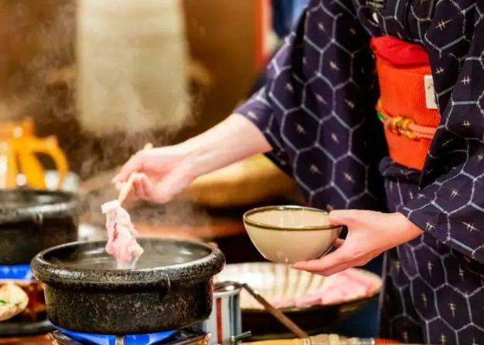 A lady in a kimono cooking thin slices of meat in a hot pot broth.